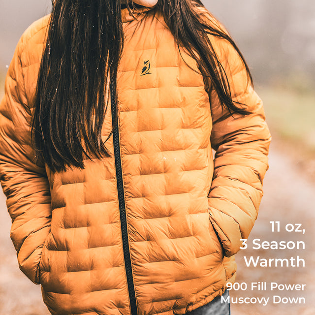 A person wearing a quilted mustard-yellow puffer jacket outdoors, with text overlay on the right reading '11 oz, 3 Season Warmth, 900 Fill Power Muscovy Down'.