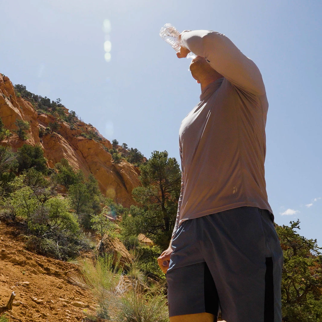 A hiker drinking water on a sunny canyon trail wearing Outdoor Vitals Skyline Trail Shorts.