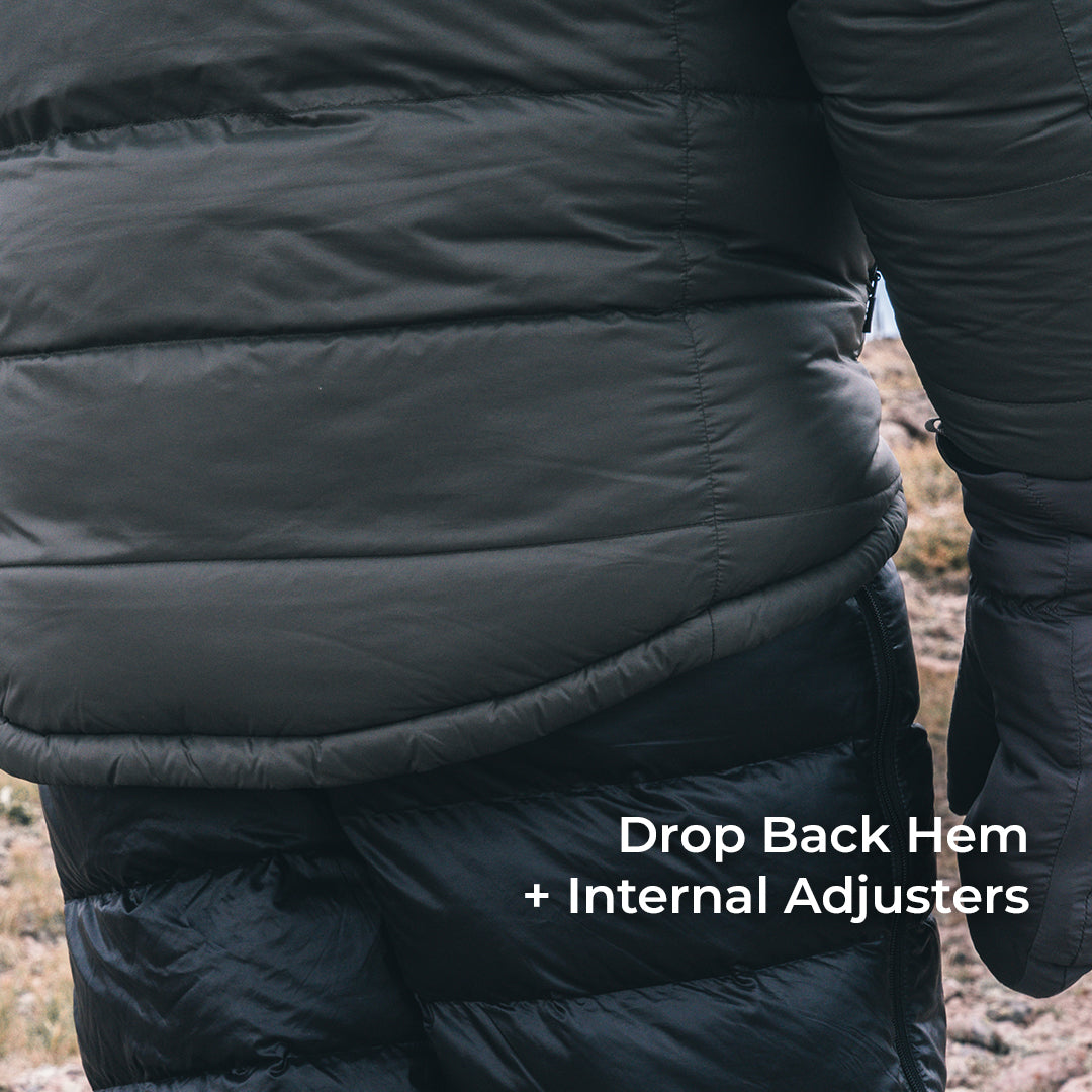 Close-up of a black puffer jacket worn outdoors, showing the lower back and hip area with text reading 'Drop Back Hem + Internal Adjusters'.