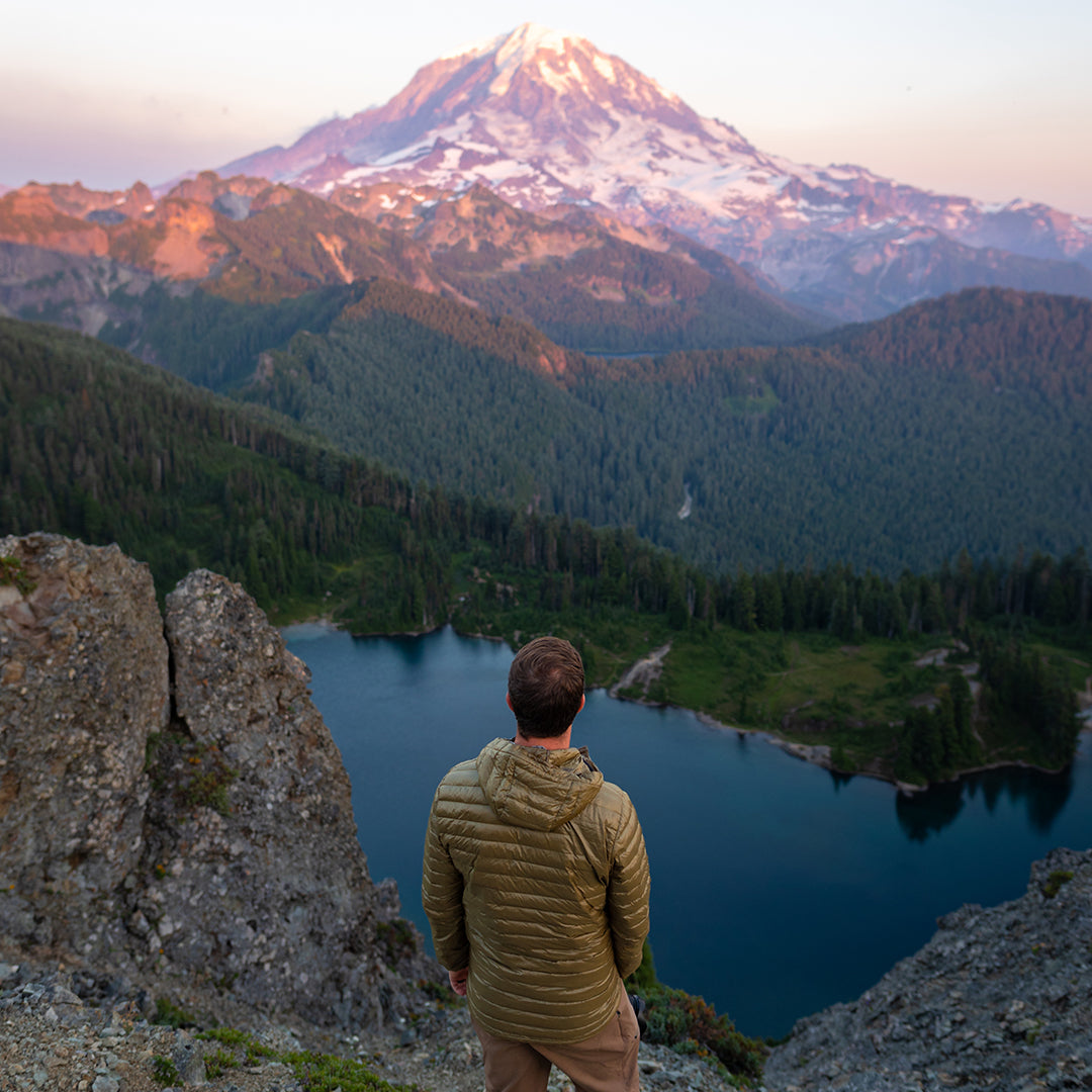 Hiker in a NovaUL down jacket overlooking a mountain lake and a massive snow-covered peak.