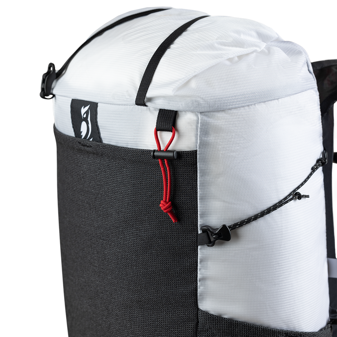 Close-up product detail of the Outdoor Vitals Skyline 30 Fastpack top section, highlighting the roll-top closure strap, brand logo patch, mesh front pocket trim, and side compression cord adjustment system.