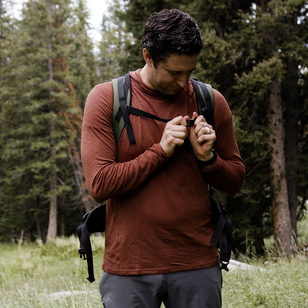 Hiker adjusting backpack strap while wearing Outdoor Vitals merino hoodie.