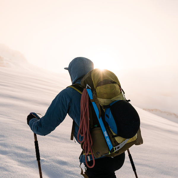 Hiker wearing the Outdoor Vitals Vario Jacket hiking toward the sun on a snow-covered mountain