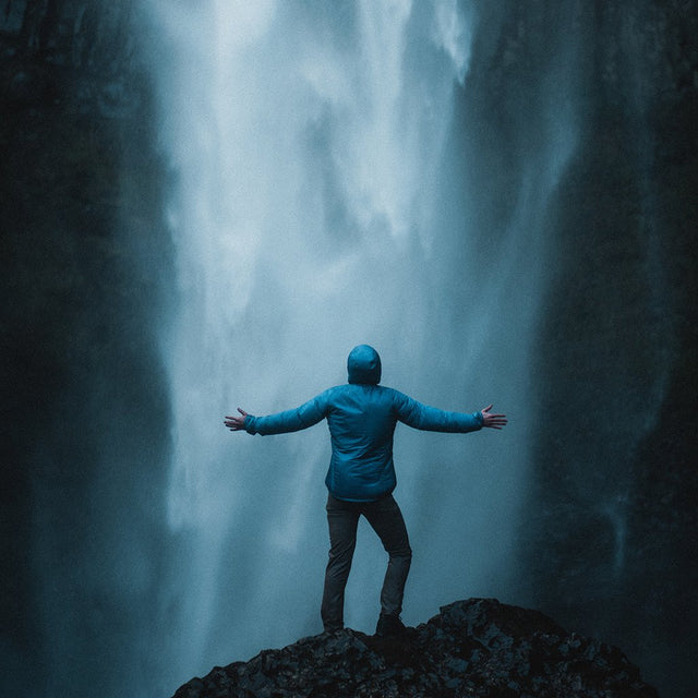 Back view of a hiker in a Ventus Active Hoodie with arms outstretched in front of a giant waterfall.