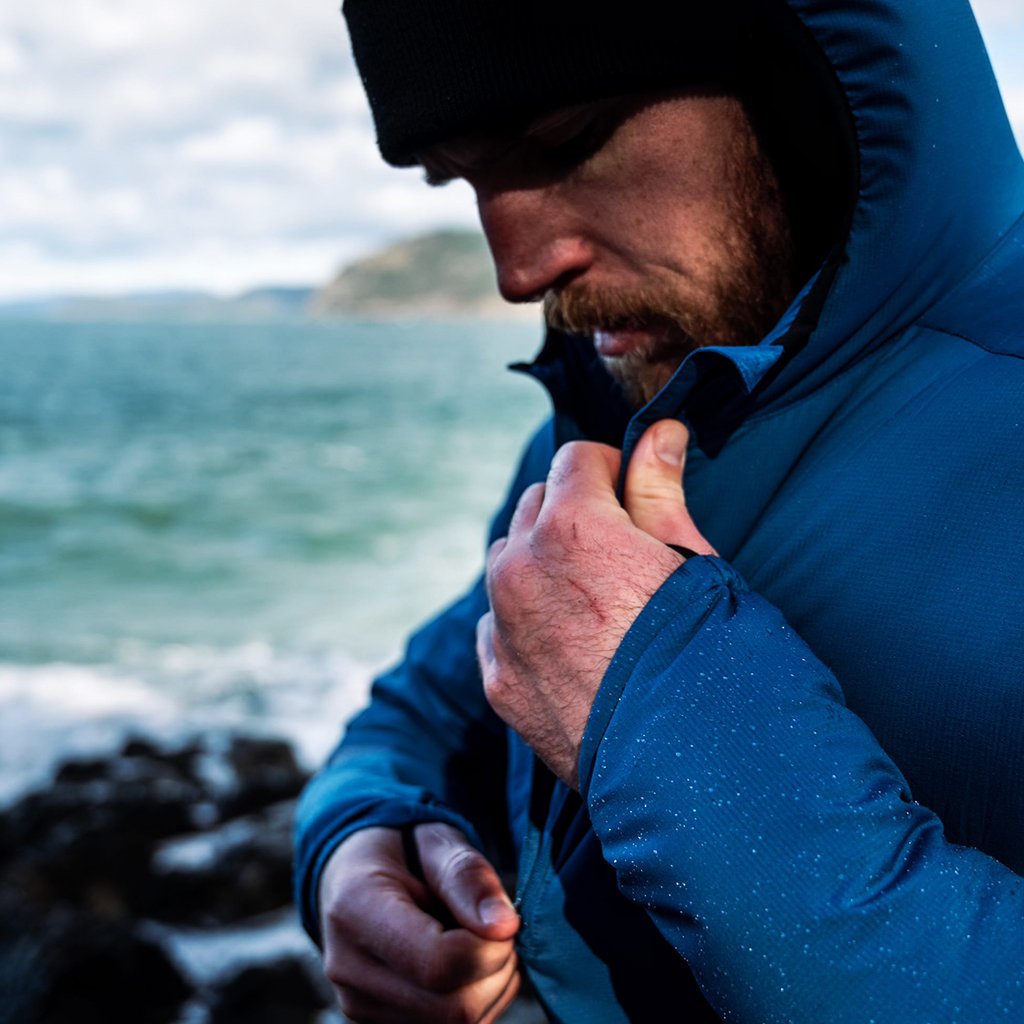 Close-up of a man adjusting a water-resistant Ventus Active Hoodie with water droplets on the sleeve by the sea.