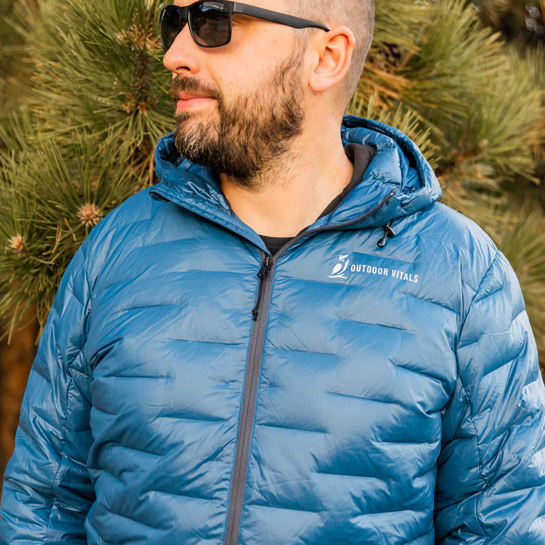 A man wearing a hooded NovaPro down jacket against a pine tree background.