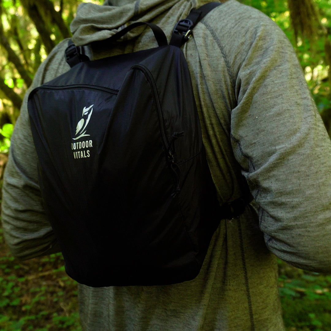 Rear view of a hiker wearing an Outdoor Vitals modular accessory pack secured to shoulder straps on an outdoor trail.
