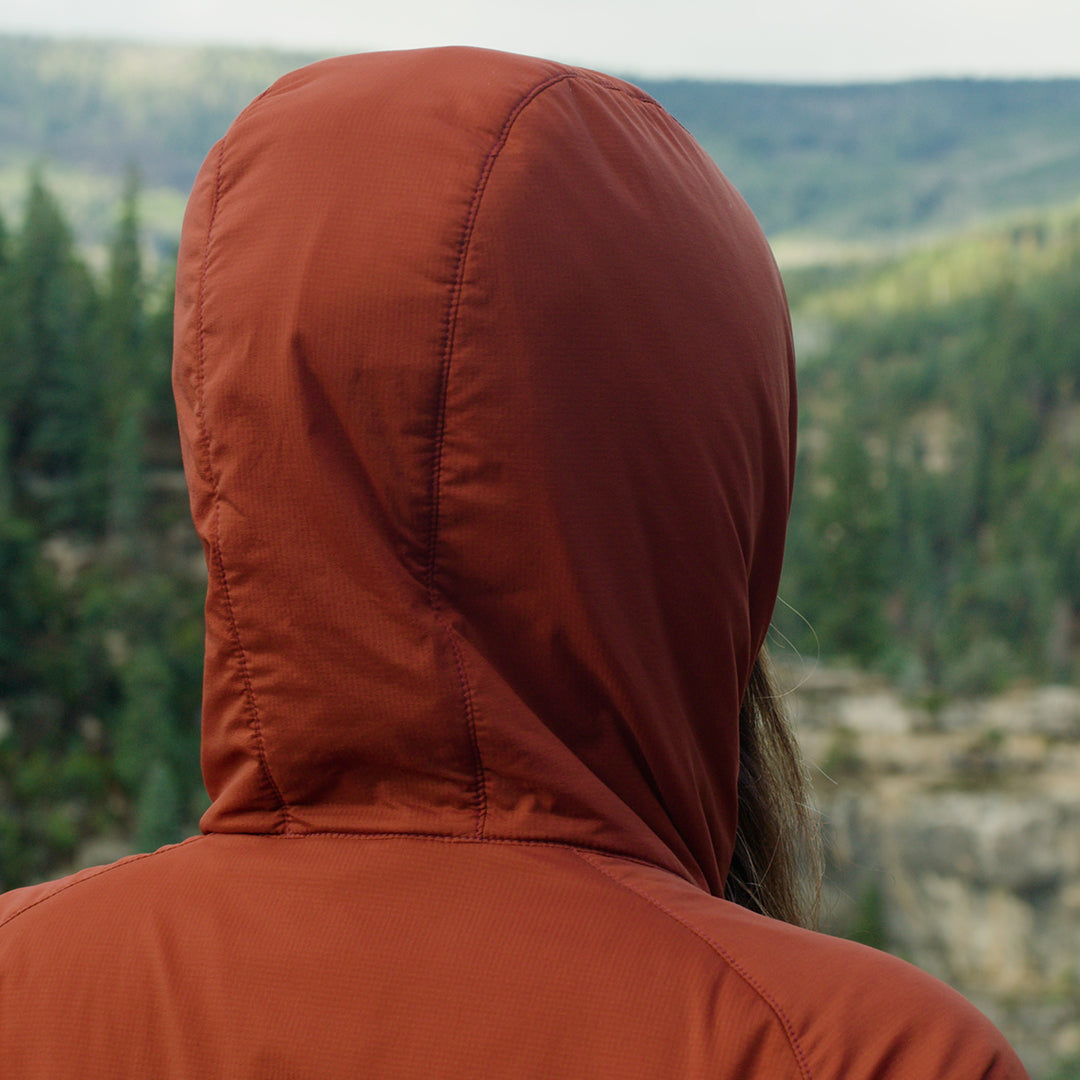 Rear view of a hiker wearing the Outdoor Vitals Vario Jacket with the hood up facing the mountains