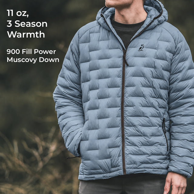 A man wearing a light blue hooded puffer jacket with a full-zip front and horizontal quilted baffles, shown outdoors against a blurred natural background. White text on the left reads '11 oz, 3 Season Warmth' and '900 Fill Power Muscovy Down'.