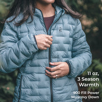 A woman wearing a light blue-gray puffer jacket outdoors, with text overlay on the right reading '11 oz, 3 Season Warmth' and '900 Fill Power Muscovy Down'.