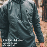 A person wearing a dark gray-green lightweight zip-front mid layer jacket outdoors in a wooded setting. White text at the bottom reads '7 oz Full Mid Layer packs to the size of a grapefruit'.
