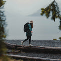 A hiker wearing a sun hat balancing on a fallen log along a misty lake shoreline while wearing the Outdoor Vitals KotaUL Ultralight Travel & Adventure Backpack.