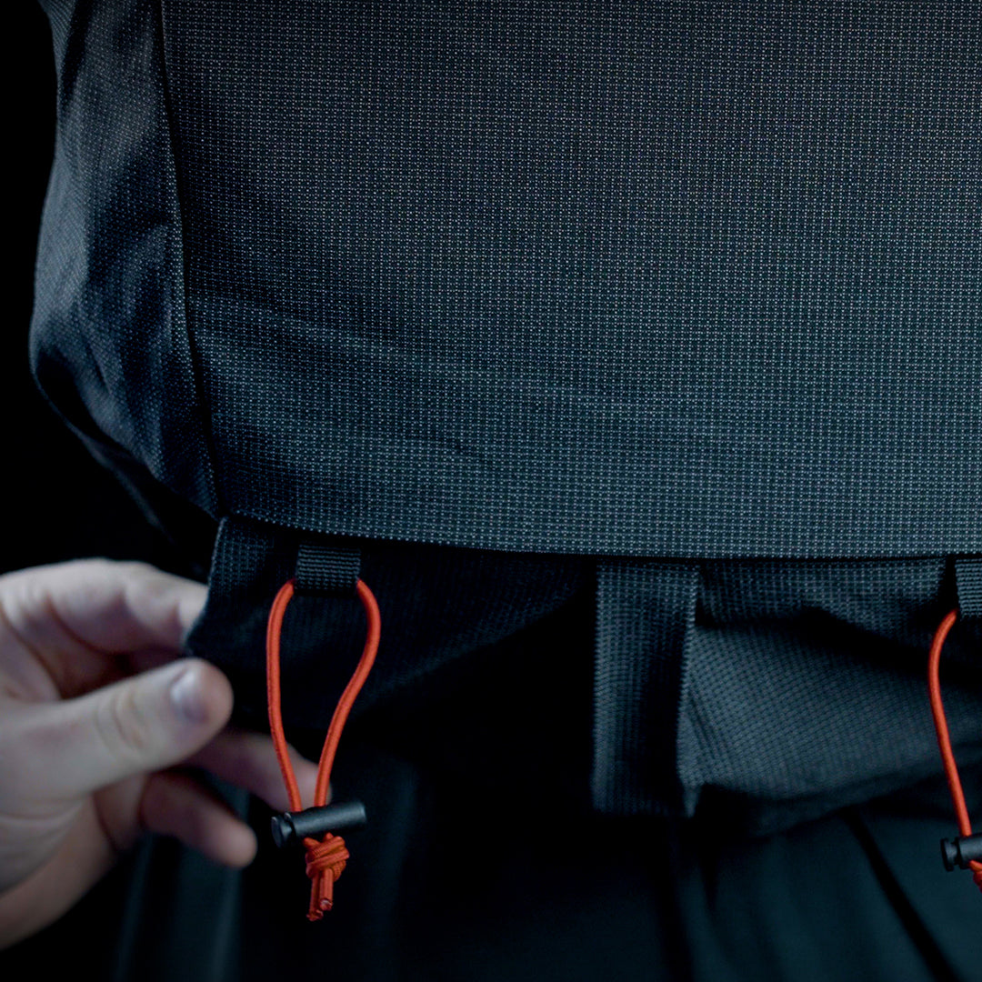 Close-up view showing a hand adjusting the bottom attachment point with elastic cord locks on the Outdoor Vitals Skyline 30 Fastpack, designed for securing gear like trekking poles or sleeping pads.