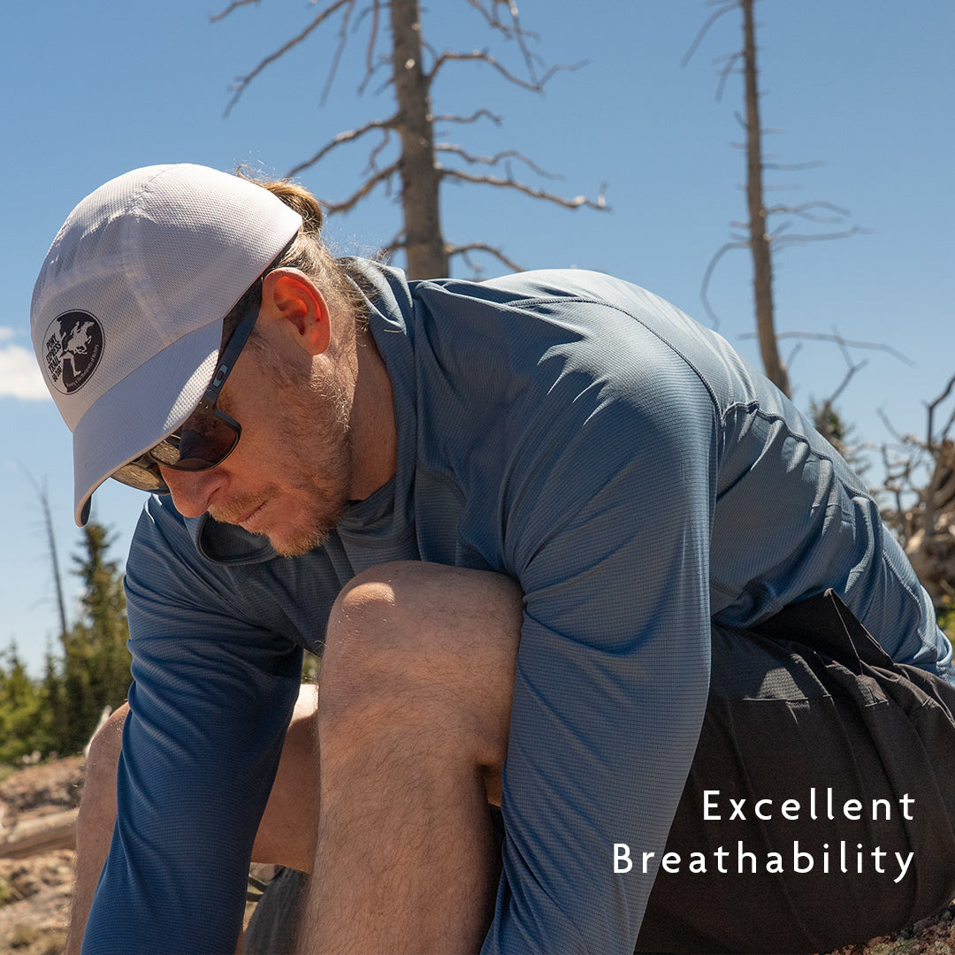 Blue - A man outdoors wearing a blue long-sleeve sun shirt, crouching in a natural setting 
