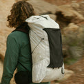 Three-quarter rear view of a hiker wearing the Outdoor Vitals CS40 Ultra Backpack on a dirt trail, highlighting the water bottle side pocket, front mesh pocket, and Y-strap compression.