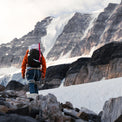 Rear view of a mountaineer trekking toward a snow-covered alpine peak while wearing the Outdoor Vitals Skyline 30 Fastpack, equipped with an ice axe strapped to the side attachment loops.
