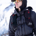Close-up front view of a mountaineer in snowy conditions wearing the Outdoor Vitals Skyline 30 Fastpack vest harness, featuring integrated flask pockets, zippered mesh compartments, and dual sternum straps.