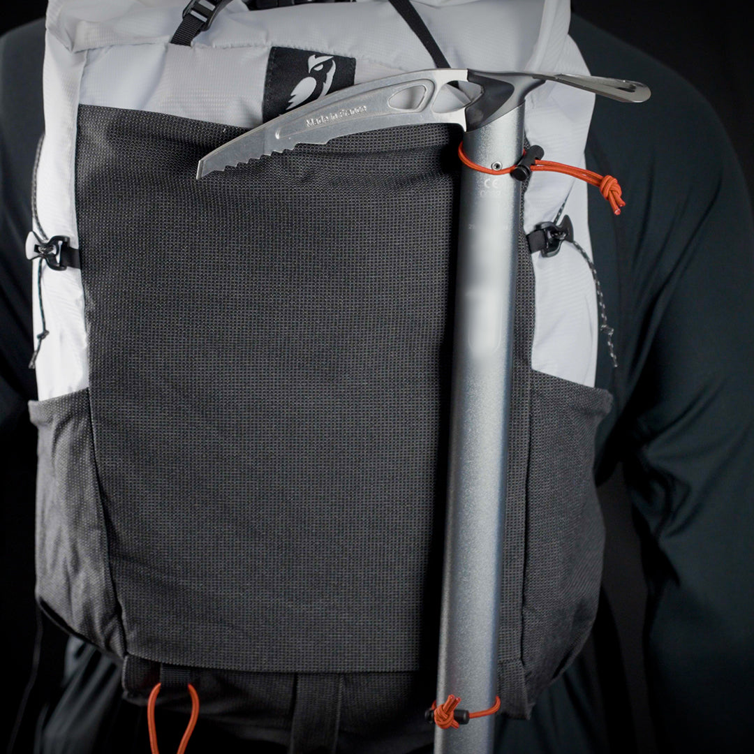 Close-up rear view of the Outdoor Vitals Skyline 30 Fastpack demonstrating an ice axe securely attached using the pack's dedicated side attachment loops and shock cord retainers.