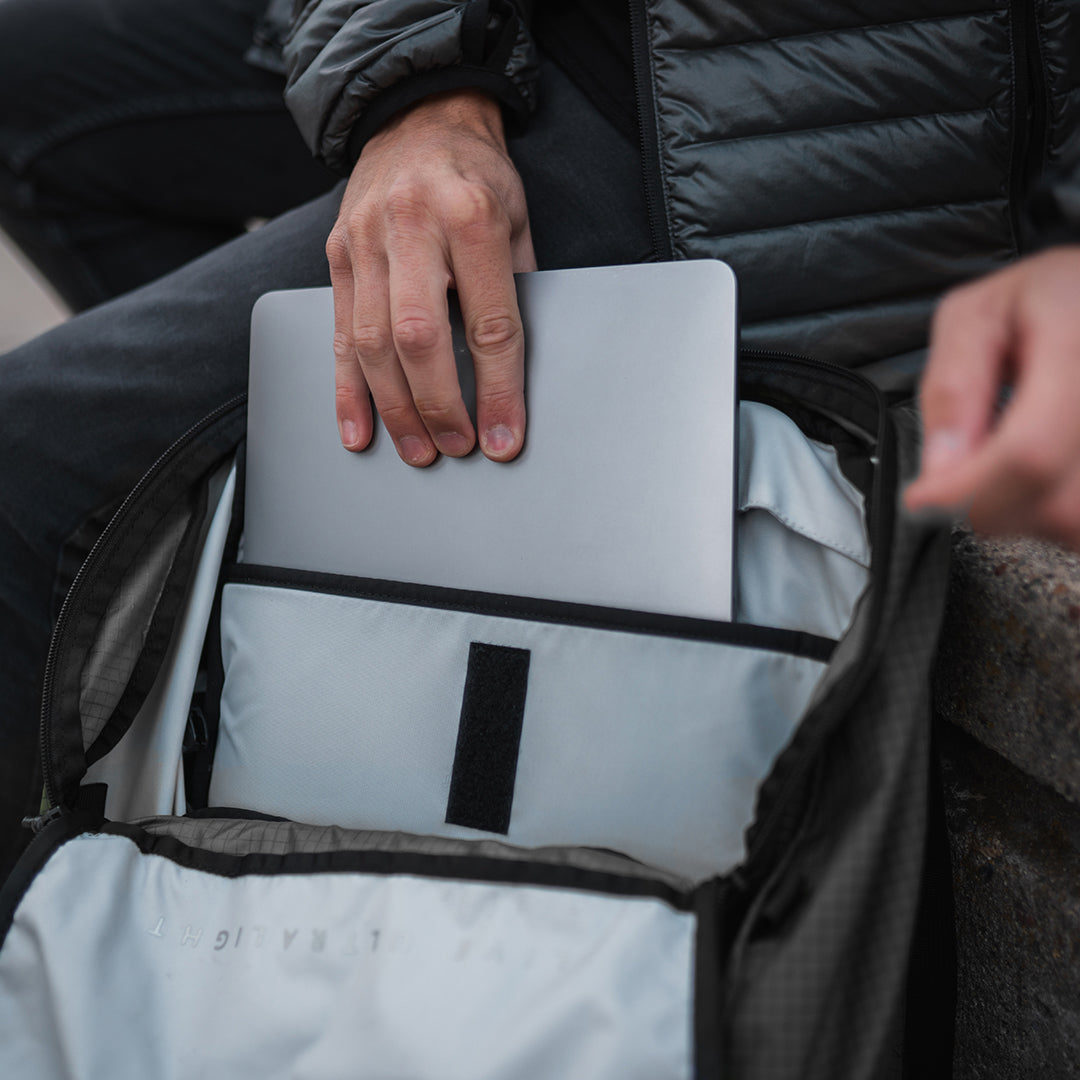 Close-up of a person sliding a laptop into the padded internal sleeve of the Outdoor Vitals KotaUL Ultralight Travel & Adventure Backpack main compartment.