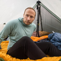 Camper inside a tent wearing merino hoodie and thermal leggings.