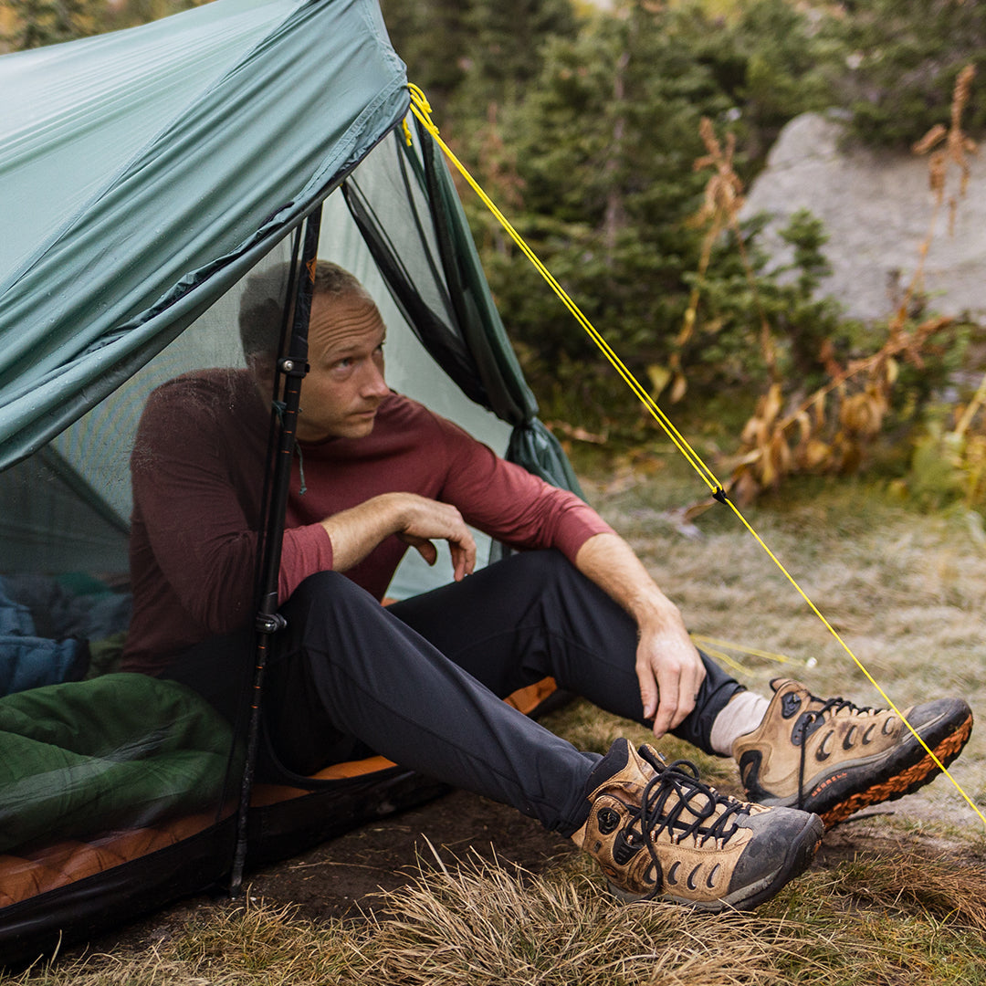 Camper sitting in a tent wearing an Outdoor Vitals merino top and thermal leggings.