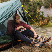 Camper sitting in a tent wearing an Outdoor Vitals merino top and thermal leggings.