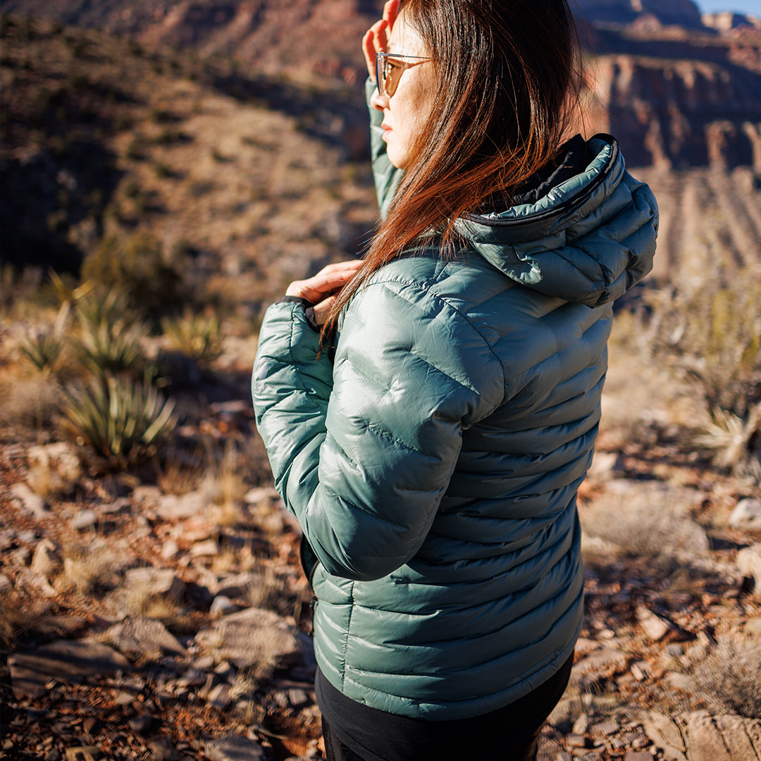 Side profile of a woman wearing a NovaPro jacket, shielding her eyes in a sunny desert canyon.