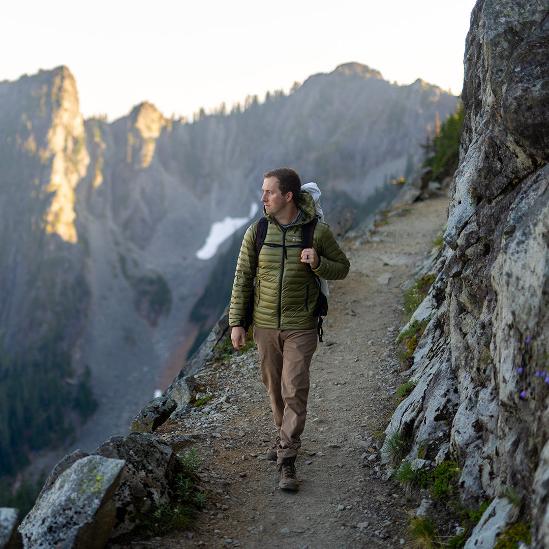 A hiker along a rocky mountain cliffside wearing a NovaUL down jacket.