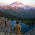 Hiker in a NovaUL down jacket overlooking a mountain lake and a massive snow-covered peak.