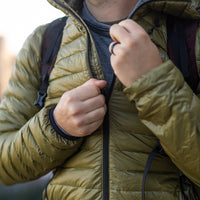 Close-up of a person zipping up a NovaUL down jacket while wearing a backpack.