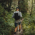 Back view of a runner fastpacking along a wooded dirt trail wearing the Outdoor Vitals Skyline 30 Fastpack, showcasing its back panel fit and compact profile.