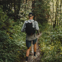 Back view of a runner fastpacking along a wooded dirt trail wearing the Outdoor Vitals Skyline 30 Fastpack, showcasing its back panel fit and compact profile.