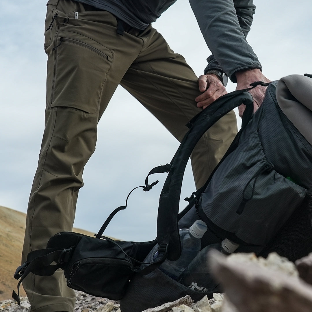 Close side view of man wearing hiking pants while picking up a backpack