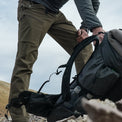 Close side view of man wearing hiking pants while picking up a backpack