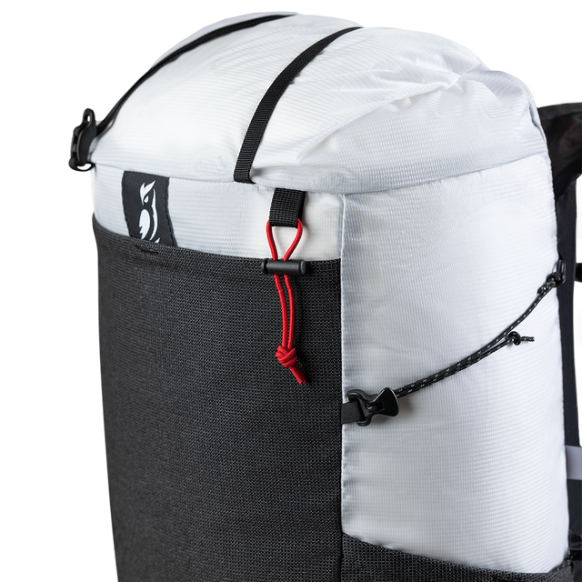 Close-up product detail of the Outdoor Vitals Skyline 30 Fastpack top section, highlighting the roll-top closure strap, brand logo patch, mesh front pocket trim, and side compression cord adjustment system.