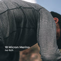 A close-up of a person wearing a long-sleeve wool athletic shirt, shown outdoors with text overlay reading '18 Micron Merino no itch'.