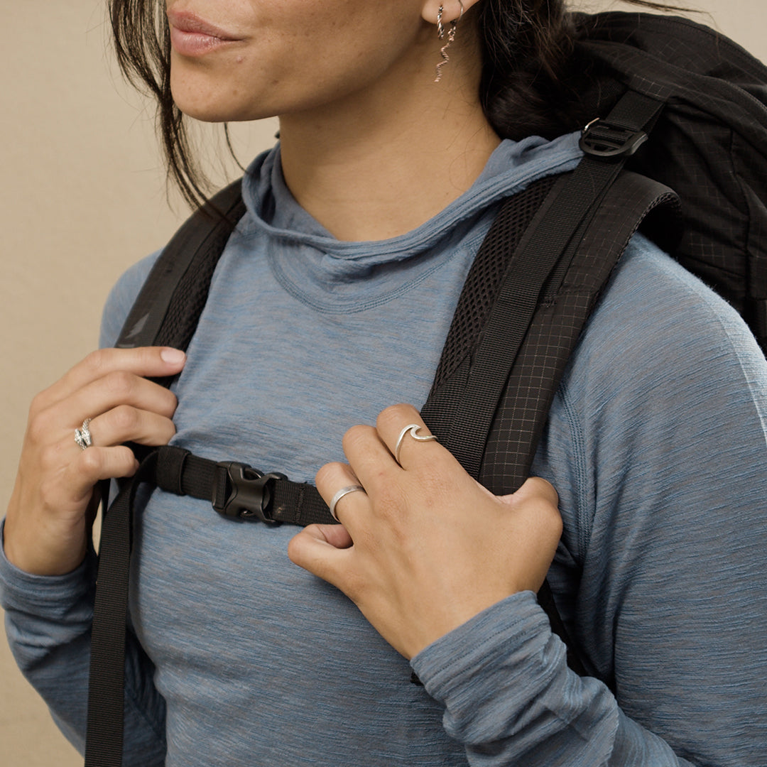 Close-up of a woman wearing Outdoor Vitals merino hoodie holding backpack straps