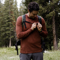 Hiker adjusting backpack strap while wearing Outdoor Vitals merino hoodie.