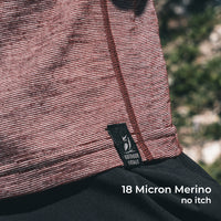 Close-up of a wool sun shirt with a black Outdoor Vitals label, worn outdoors with blurred greenery in the background. White text at the bottom reads '18 Micron Merino no itch'.