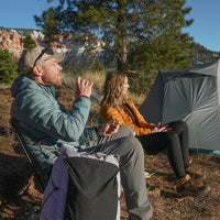 Man and woman wearing insulated Zulu down jackets relaxing at a campsite beside a backpacking tent.