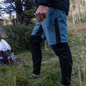Lower-body view of a male hiker wearing Outdoor Vitals Highline Thermal Leggings layered under athletic shorts while standing in a grassy outdoor environment.
