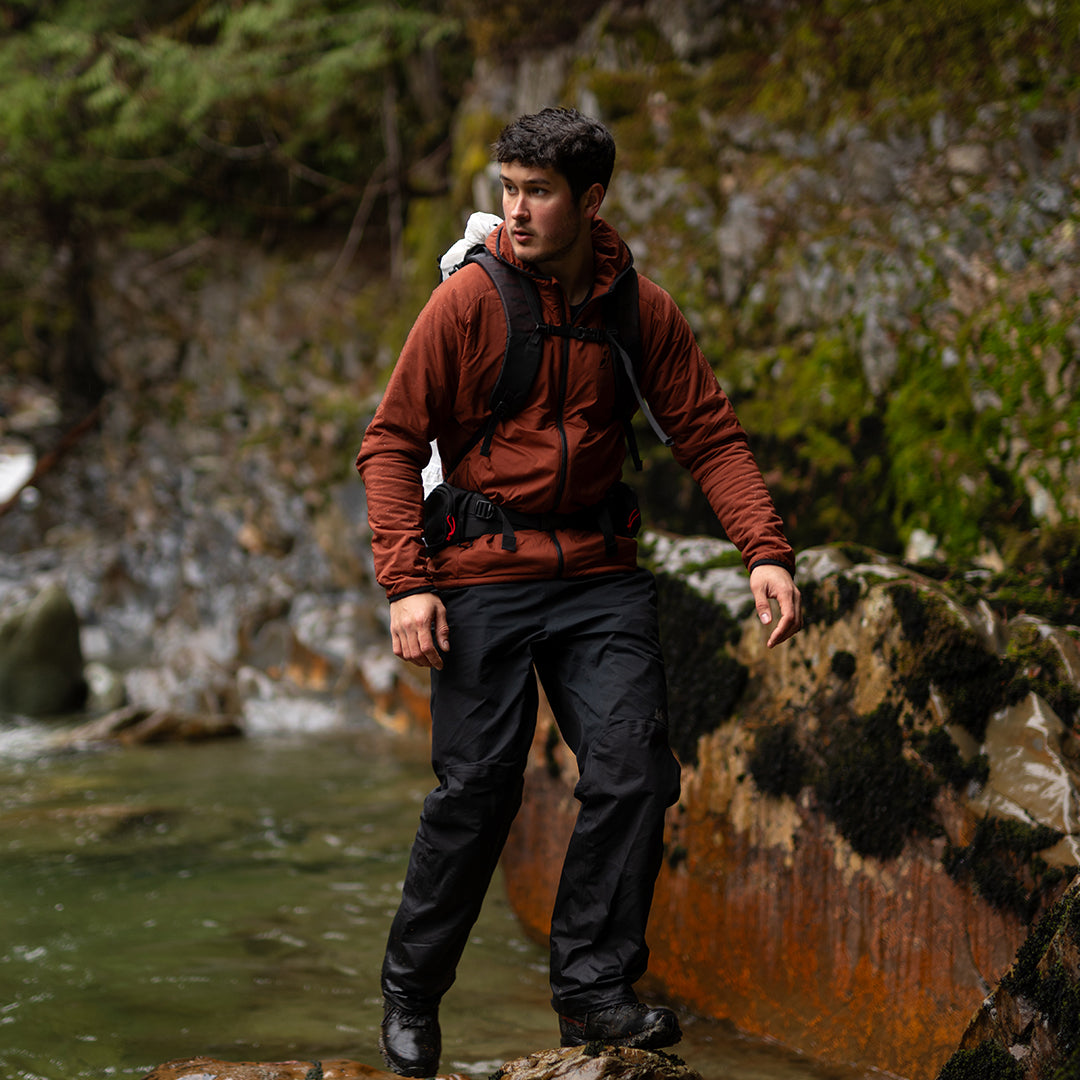 Hiker wearing the Outdoor Vitals Vario Jacket crossing a rocky mountain river