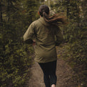 Back view of a woman trail running in a Ventus Active Hoodie through a wooded forest path.
