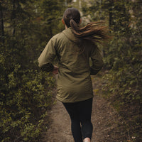 Back view of a woman trail running in a Ventus Active Hoodie through a wooded forest path.