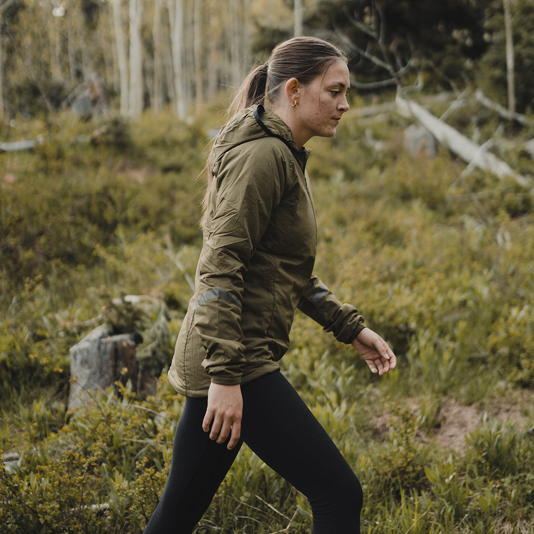 Woman in an hooded jacket and black leggings walking on an outdoor trail.