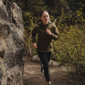 Woman running on a wooded trail next to a rock wall, wearing an Ventus Active Hoodie and leggings.