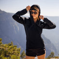 Hiker wearing a hooded activewear top and shorts on a sunny mountain trail.