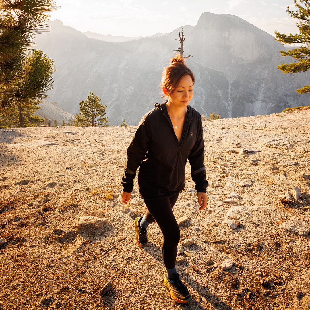Woman walking on a sunny mountain summit trail wearing a lightweight hooded jacket