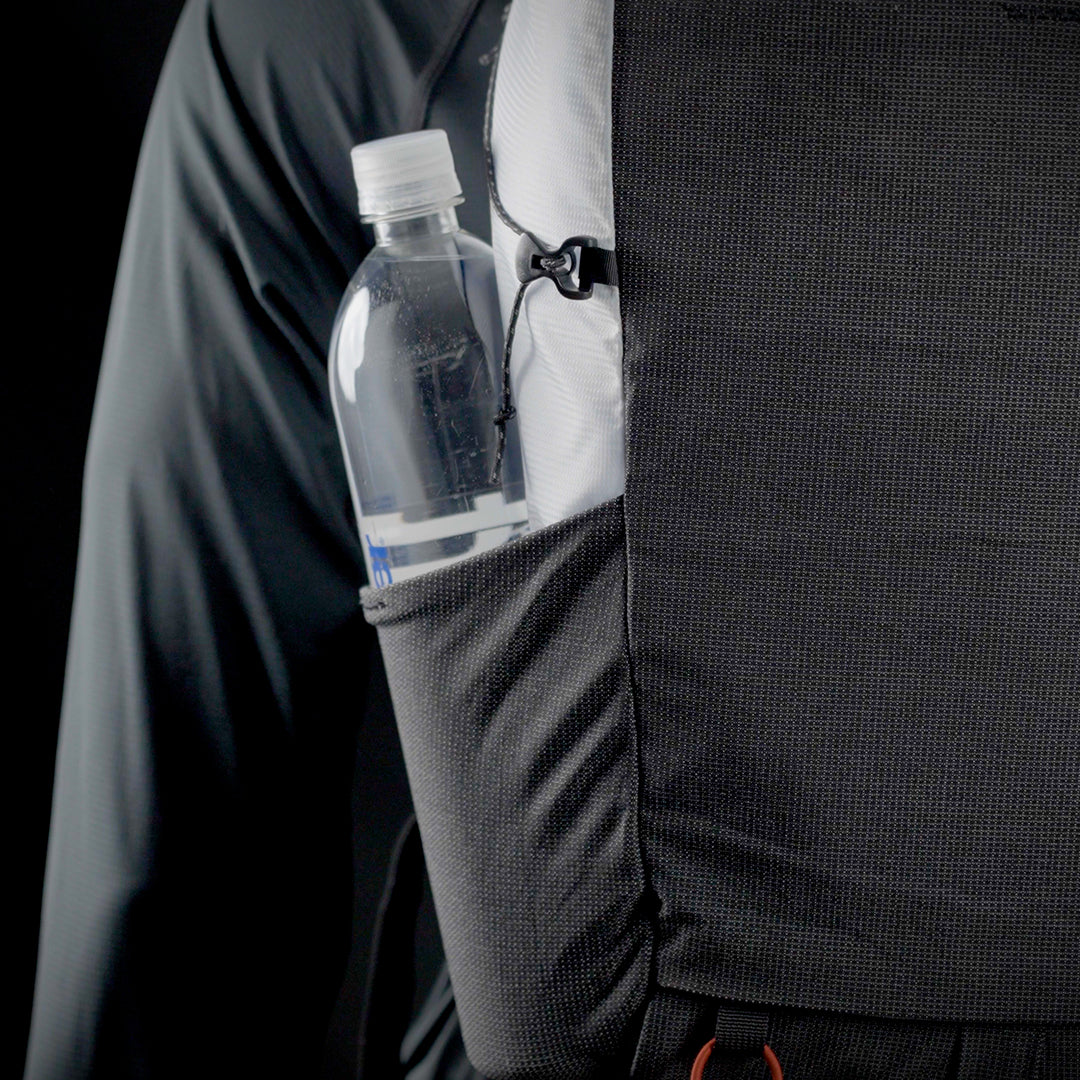 Close-up side view of the Outdoor Vitals Skyline 30 Fastpack showing a water bottle stored in the side stretch-woven pocket with cinch adjustment for secure carry.
