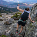 Rear view of a hiker scrambling over rocky mountain terrain wearing the Outdoor Vitals Skyline 30 Fastpack, showing the secure fit during technical movement and scenic valley views below.